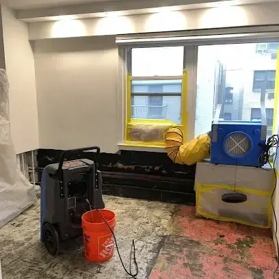 A dehumidifier and an air mover running side by side in a home room where the old flooring has been removed